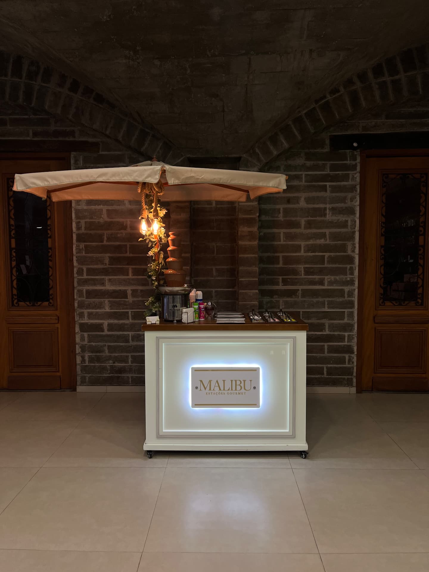 Estação gourmet com cascata de chocolate montada em espaço de eventos com parede de tijolos