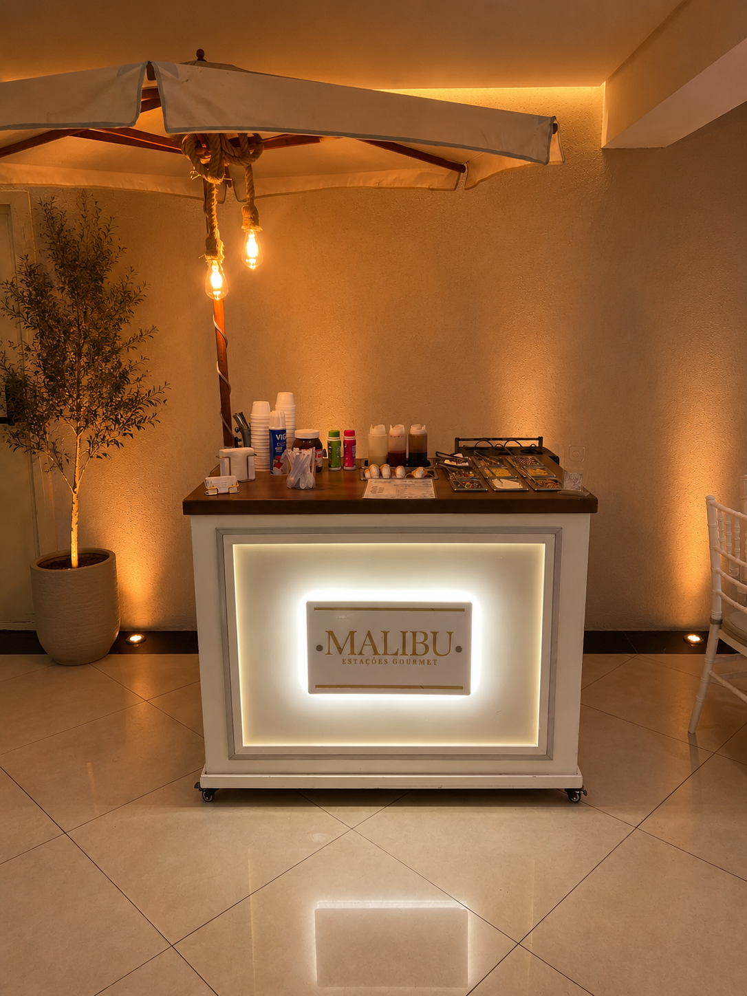 Estação gourmet da Malibu montada em salão de festas com iluminação aconchegante